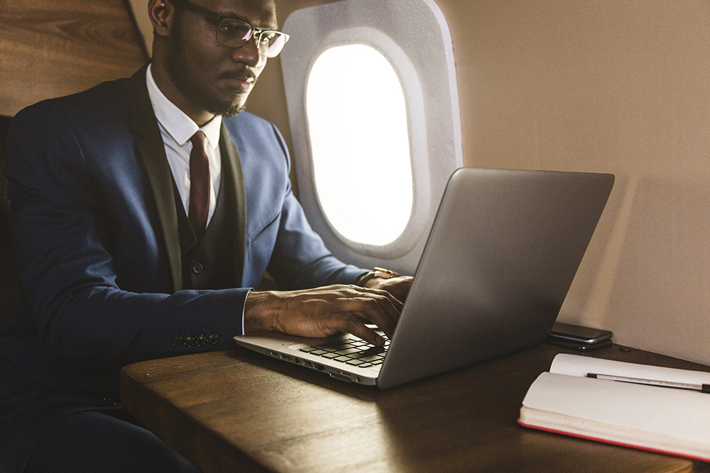 Attractive and successful African American businessman with glasses working on a laptop while sitting in the chair of his private jet. donors private client services | the giving block